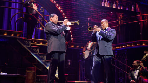 2 men in suits playing their trumpets towards each other.