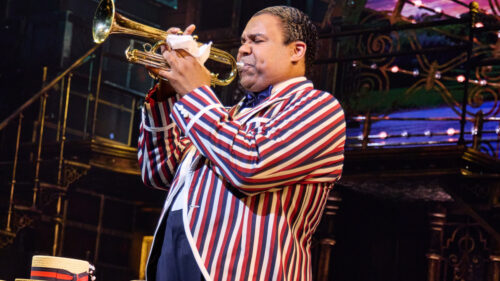 A man in a striped jacket playing the trumpet enthusiastically.